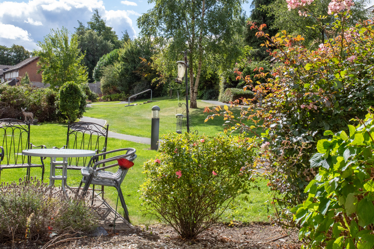 Landscaped communal garden with outdoor seating, colourful planting, winding pathways and mature trees, providing a peaceful outdoor space for residents.