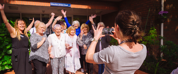 Group picture of residents having their photo taken smiling with their arms in the air