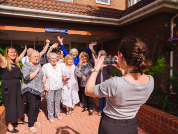 Group picture of residents having their photo taken smiling with their arms in the air