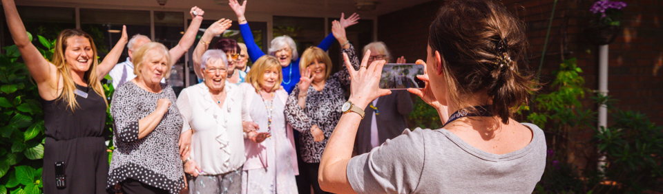 Group picture of residents having their photo taken smiling with their arms in the air 