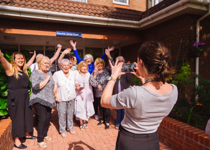 Group picture of residents having their photo taken smiling with their arms in the air