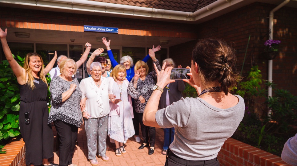 Group picture of residents having their photo taken smiling with their arms in the air
