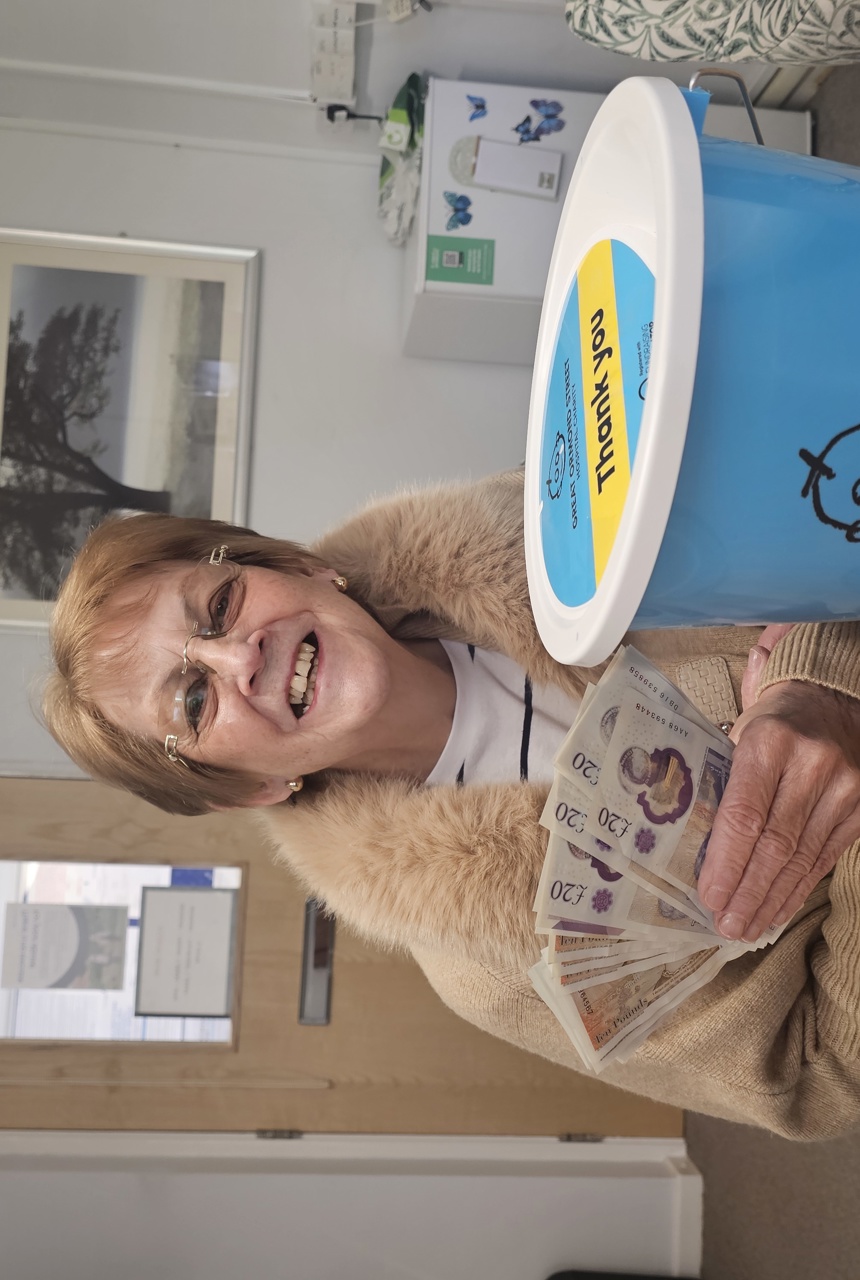 Smiling lady holds cash and charity bucket