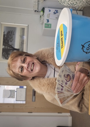 Smiling lady holds cash and charity bucket