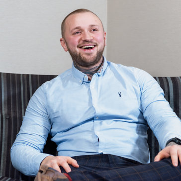 An employee wearing office attire sits on a sofa and laughs