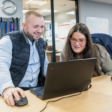 Two Housing 21 colleagues look intently at a laptop whilst working from an Extra Care scheme