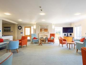 Large residents' lounge with seating, tables and a large TV and fireplace