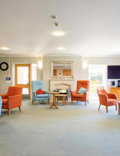 Large residents' lounge with seating, tables and a large TV and fireplace 