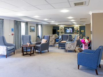 Inside the communal lounge of Oakwood Gardens with light grey carpet and blue arm chairs 