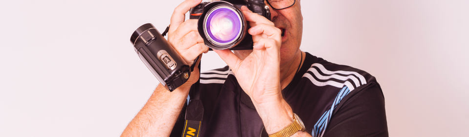Housing 21 resident wearing a baseball cap and glasses looking through the lens of a camera 