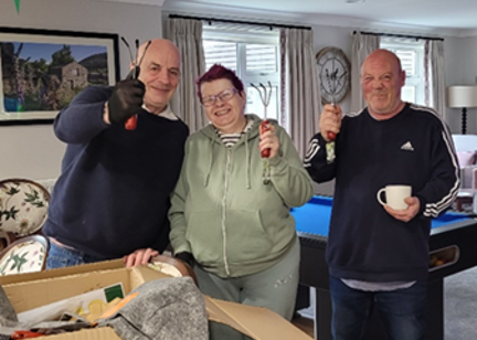 Three residents at Bannister Court holding up gardening tools