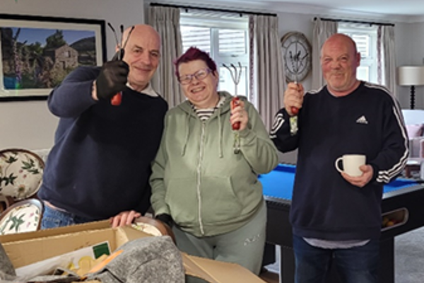 Three residents at Bannister Court holding up gardening tools