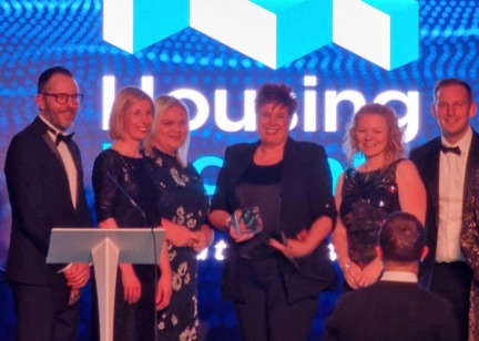 Group of Housing 21 employees dressed in suits on stage collecting a glass award
