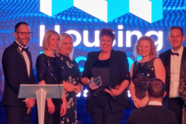 Group of Housing 21 employees dressed in suits on stage collecting a glass award