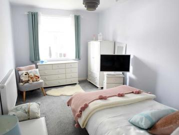 A photo of a single bedroom at Goodman Court with a bed, TV, storage units and bright window