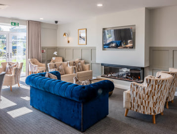 The residents' lounge with large soft seating, fireplace and wall-mounted TV