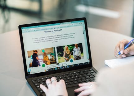 A laptop open on a table showing an image of the Housing 21 website. 