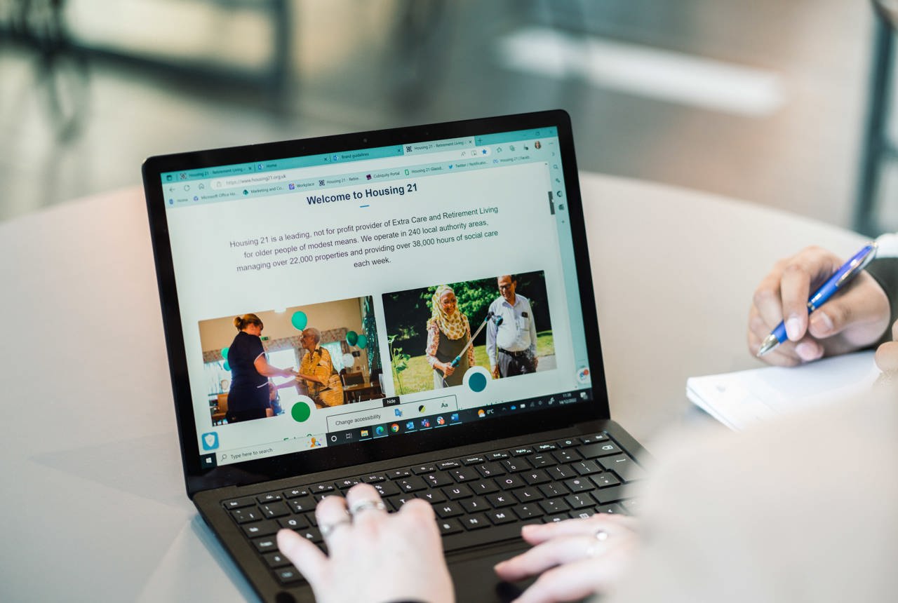 A laptop open on a table showing an image of the Housing 21 website. 