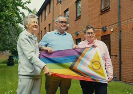 Three residents hold LGBTQ+ flag