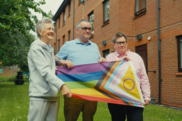 Three residents hold LGBTQ+ flag