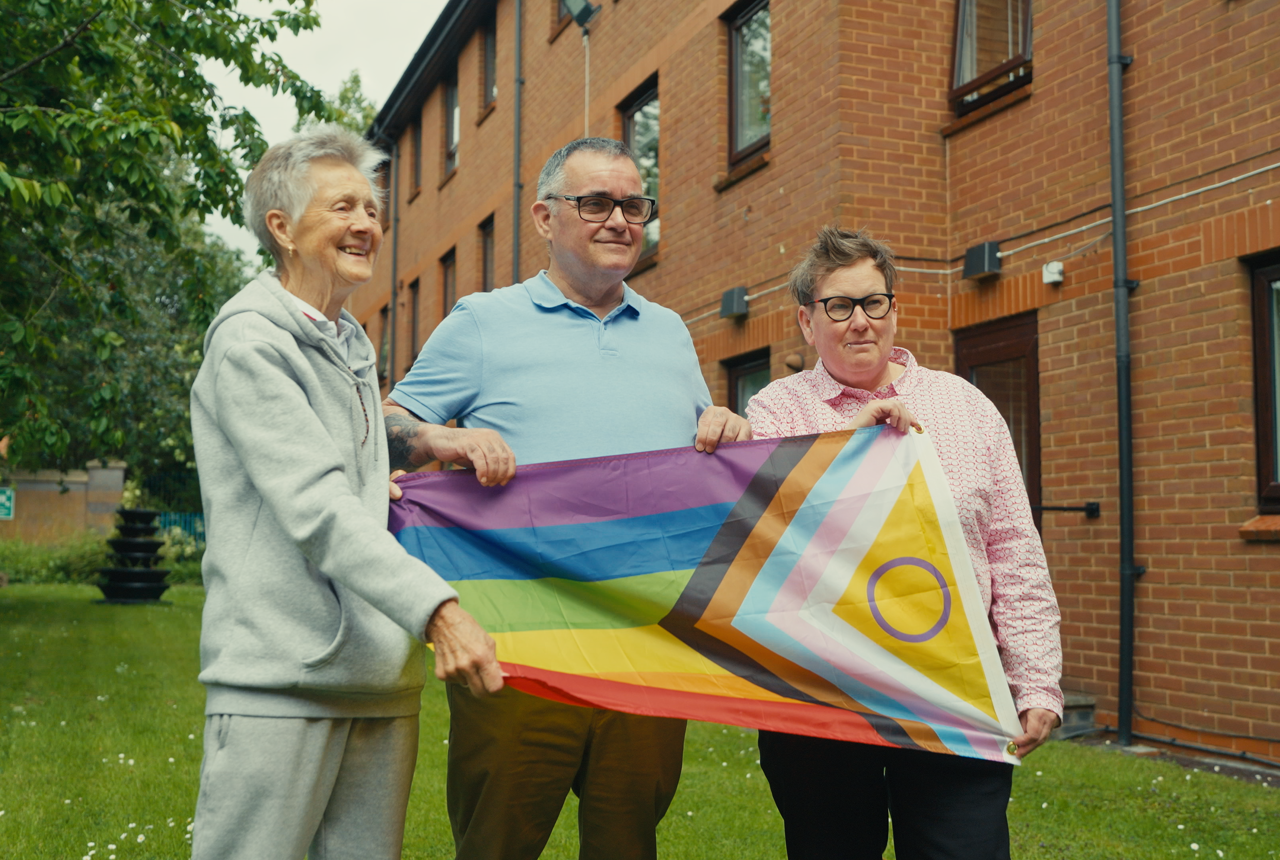 Three residents hold LGBTQ+ flag