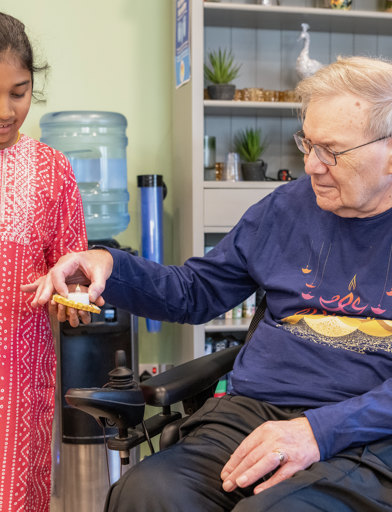 Elderly resident in a wheelchair takes a candle from a child at a colourful Diwali celebration 