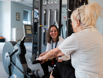 A resident using the rowing machine in the on-site gym with help from an employee