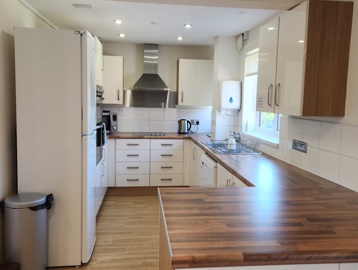 A communal kitchen, modern wooden work surfaces, and clean white cupboards