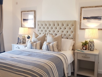 Bedroom featuring a beige double bed with blue and white stripped duvet cover with pillows. Featuring two bed side tables with lamps