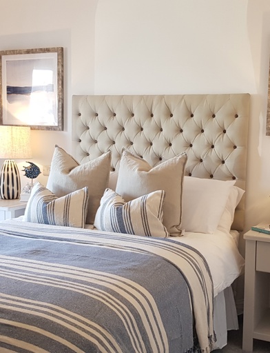 Bedroom featuring a beige double bed with blue and white stripped duvet cover with pillows. Featuring two bed side tables with lamps 