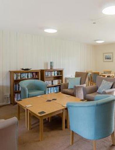 Residents' lounge with soft seating and coffee tables, and a selection of books on book shelves 