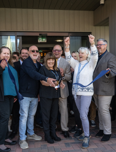 A group of residents, Housing 21 colleagues, celebrating as the ribbon is being cut 