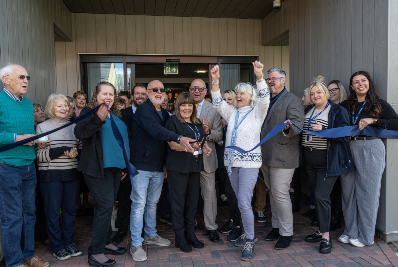 A group of residents, Housing 21 colleagues, celebrating as the ribbon is being cut
