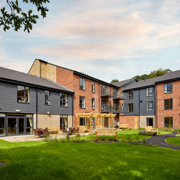 The exterior of a three-storey building surrounded by a lawn, outdoor seating and patio