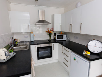 A modern kitchen with white walls and cupboards and black countertops