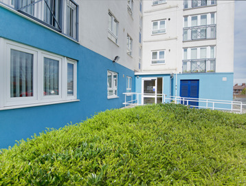 Ramp leading up to side entrance of scheme with green hedgerow under windows