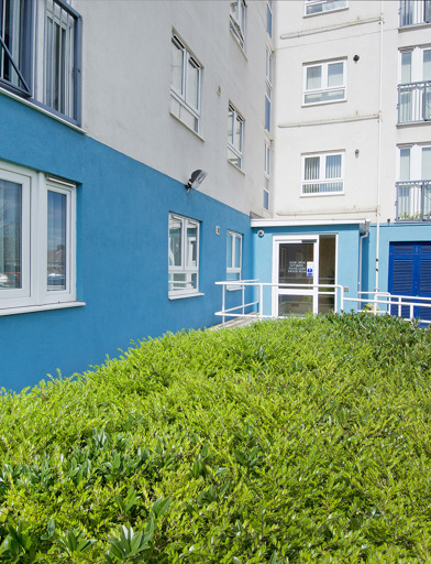 Ramp leading up to side entrance of scheme with green hedgerow under windows